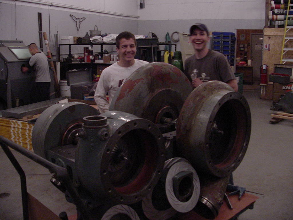 Chris Fischer and his younger brother David smiling behind the industrial air compressor they were building in a machine shop