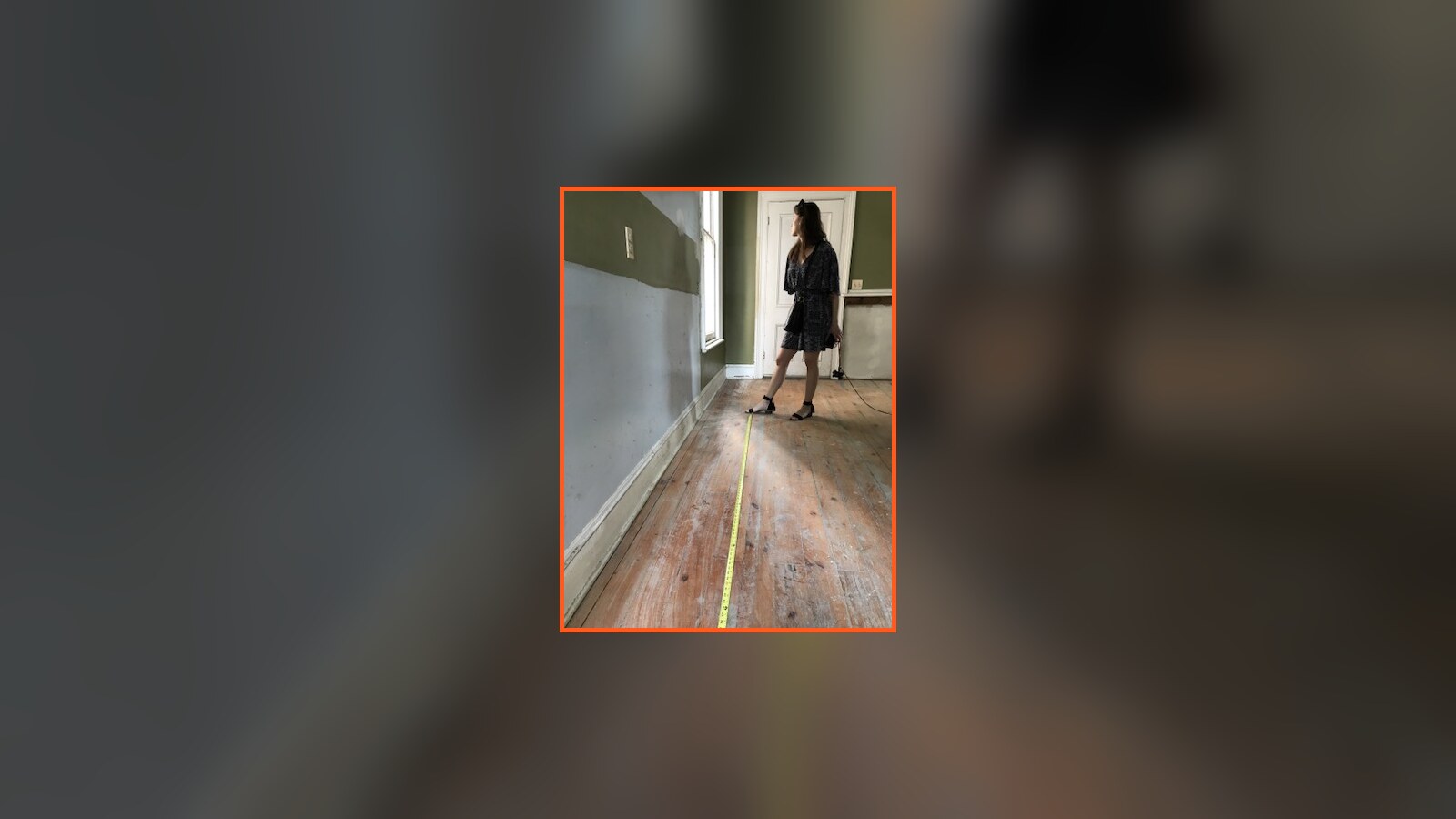 Amanda standing in an unfinished room of the Poughkeepsie Victorian while a tape measure runs across the floor