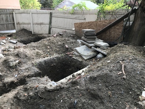 Open drainage trenches, removed pavers, and piles of soil behind the Poughkeepsie house