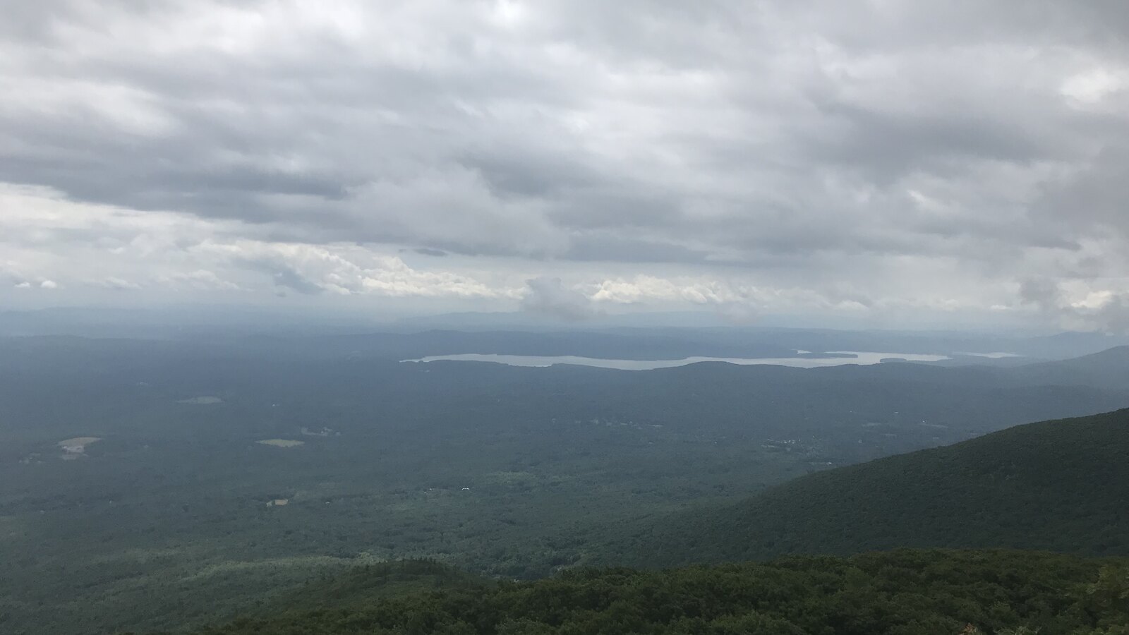 Clouds hanging over a green Catskills valley and distant lake from a mountain ridge