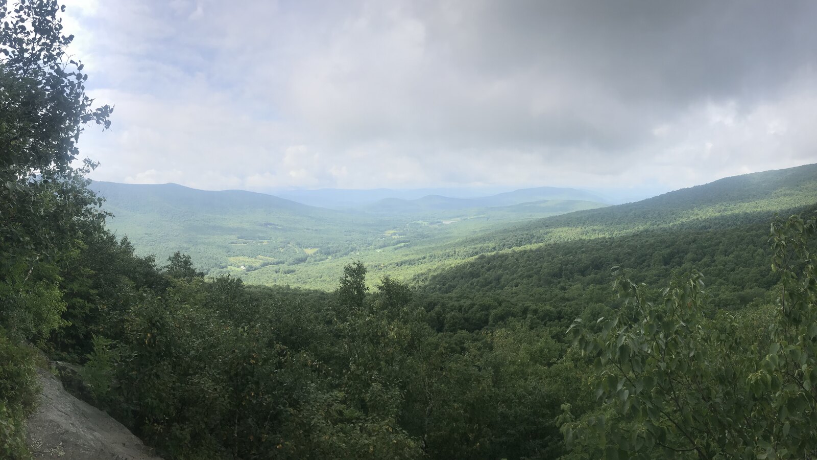 A green Catskills valley under dark rain clouds, seen from a rocky overlook