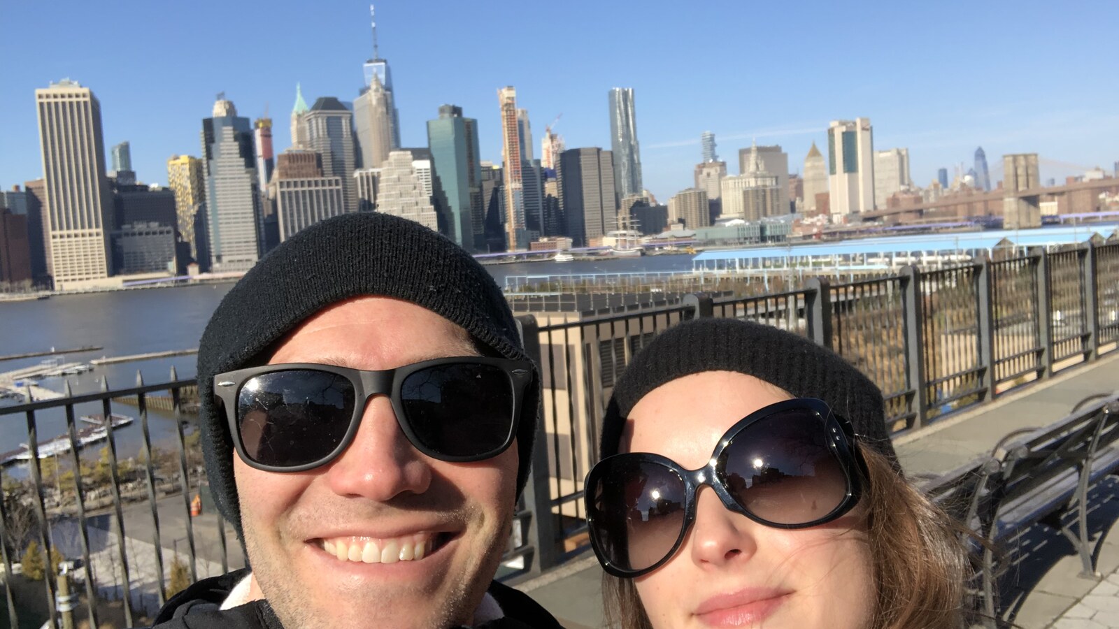 Chris and Amanda in winter hats on the Brooklyn Heights Promenade with Lower Manhattan behind them