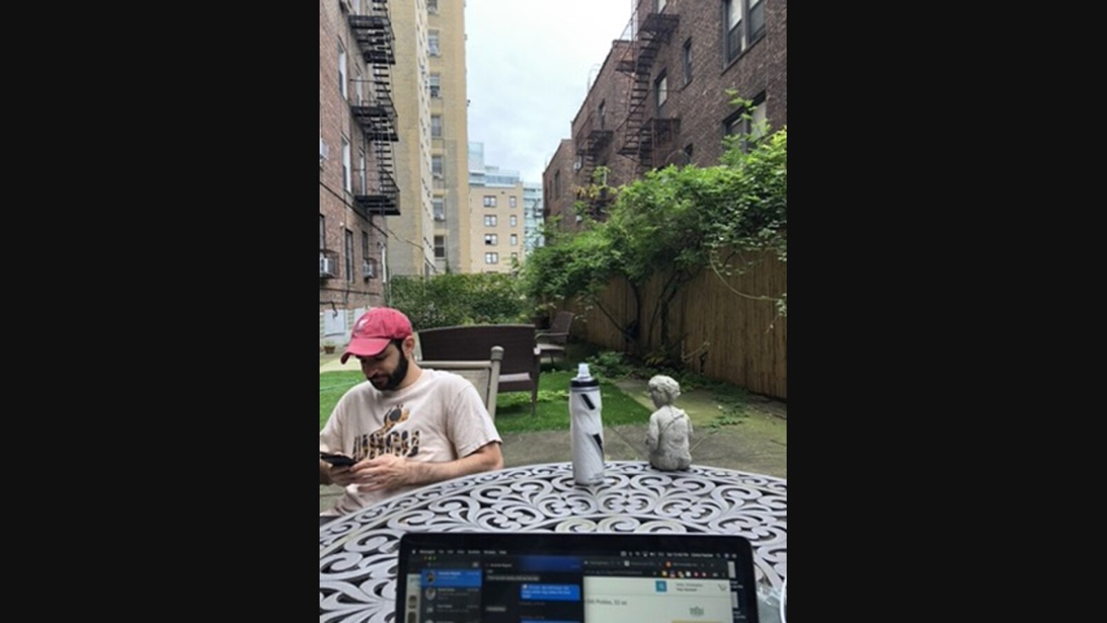 Chris sits outside looking at his phone with an open laptop in the foreground