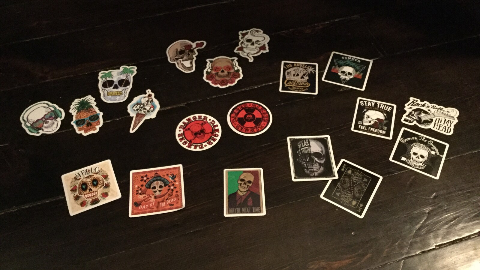 A group of skull and summer themed sticker samples spread across a dark wood floor