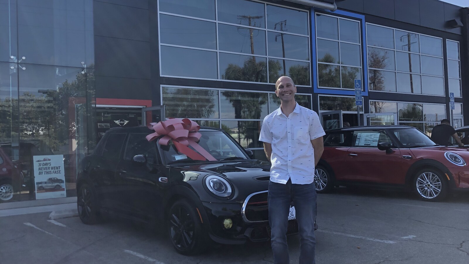 Chris Fischer smiling beside a black Mini with a large pink bow after moving to Newport Beach
