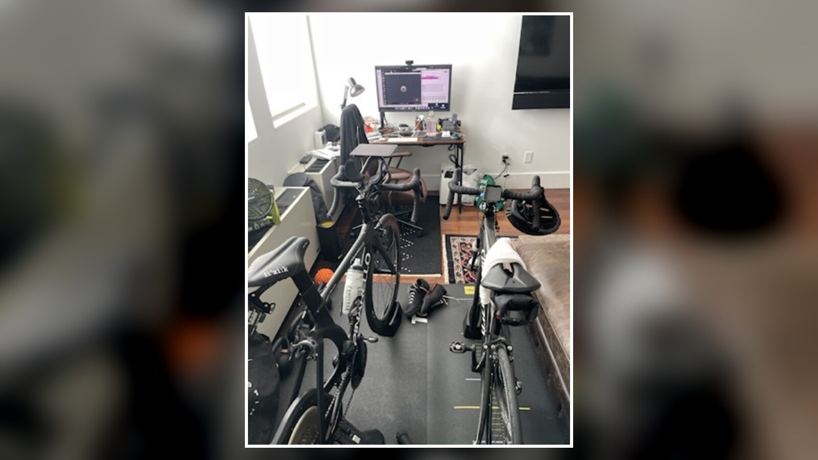 Three bicycles on indoor trainers beside a small desk and computer