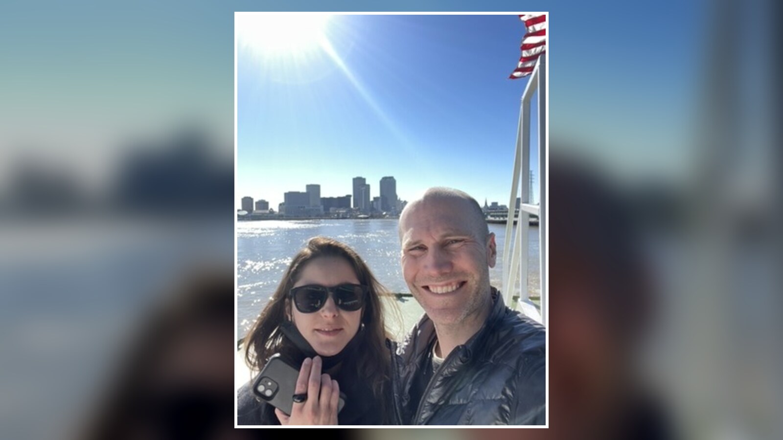 Chris Fischer and Amanda Wigand smiling on a boat with New Orleans across the water