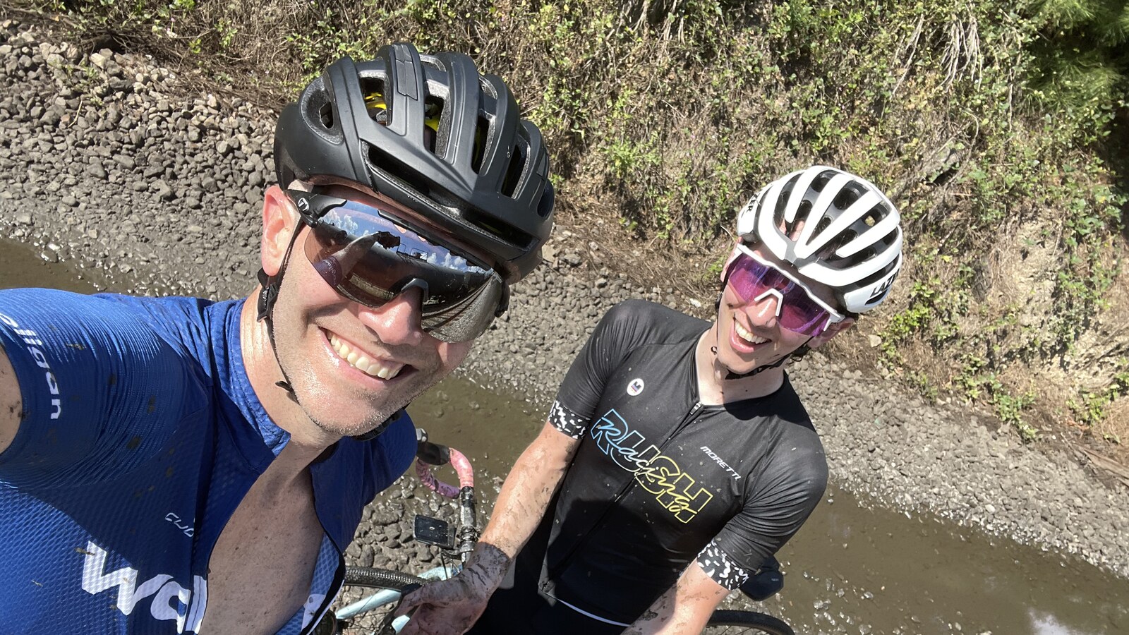 Chris and a friend smiling beside their mud-covered bikes during a rough Saturday ride