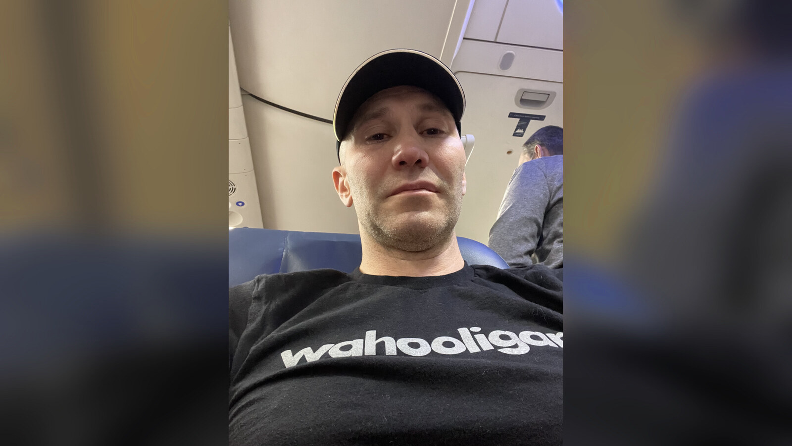 Chris sitting on a plane in a black Wahooligan shirt the evening the pizzeria idea arrived