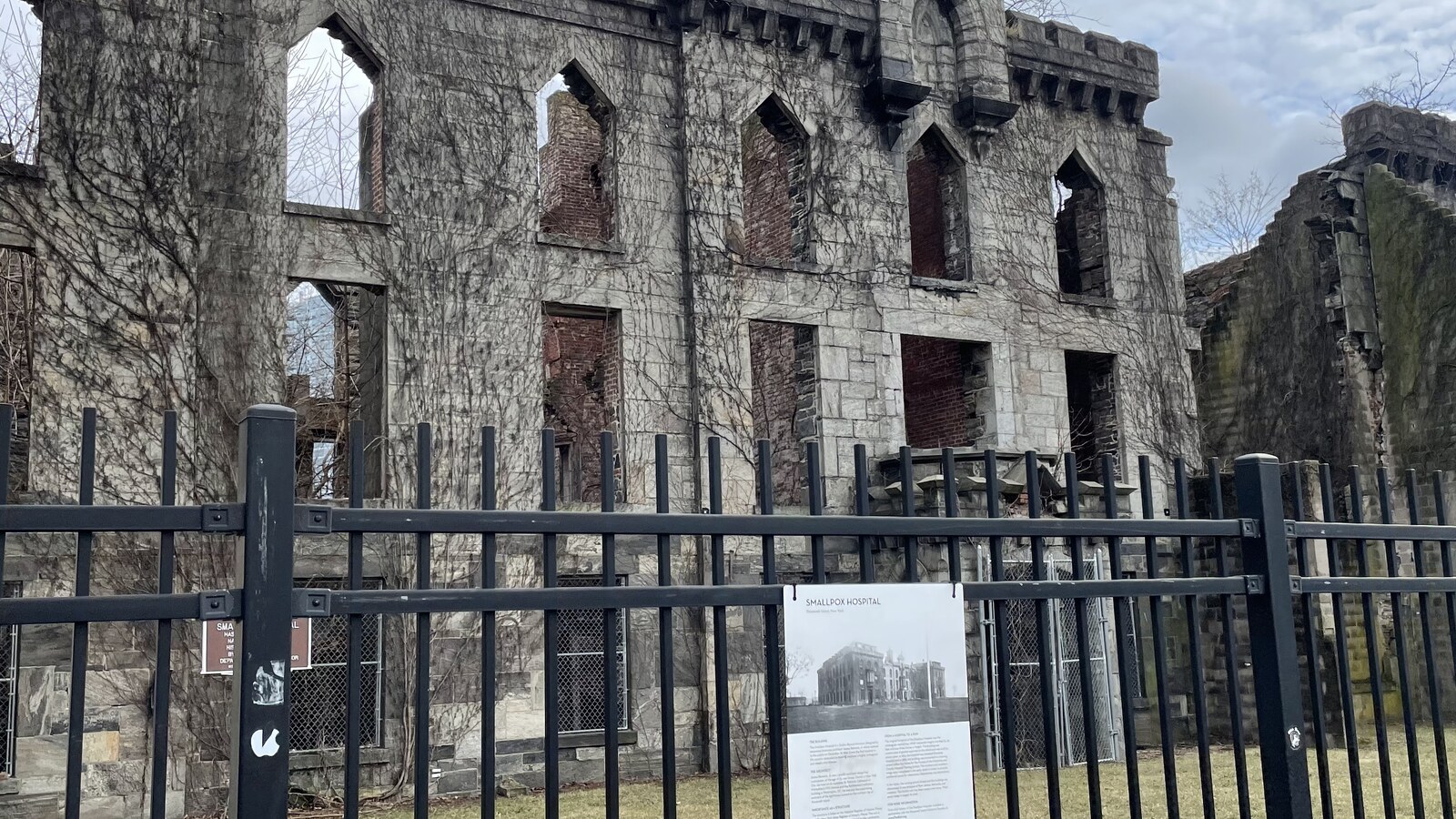 The roofless stone Smallpox Hospital ruin behind a black fence on Roosevelt Island