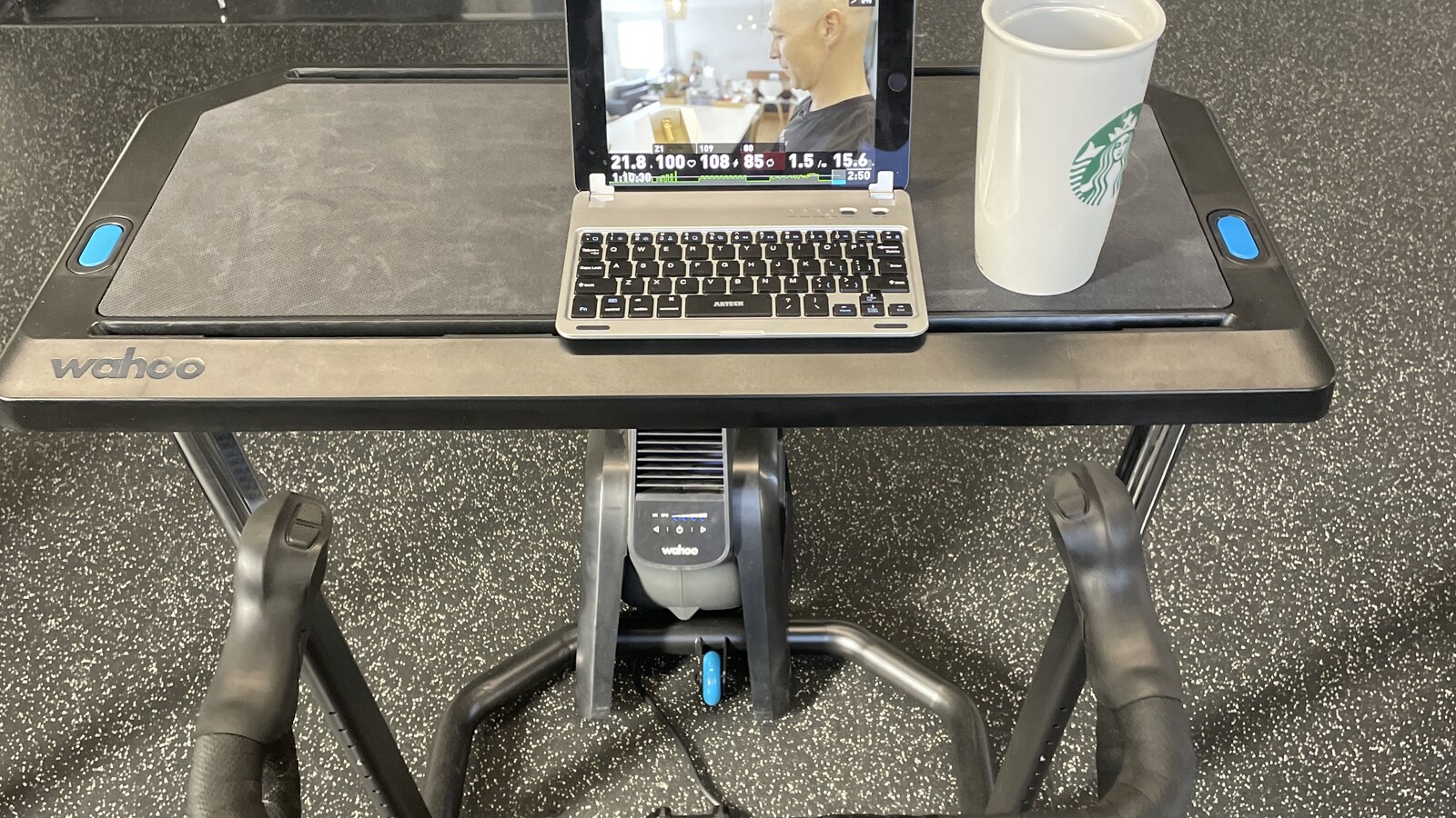 A small laptop and coffee cup on a Wahoo KICKR Desk above an indoor bicycle trainer