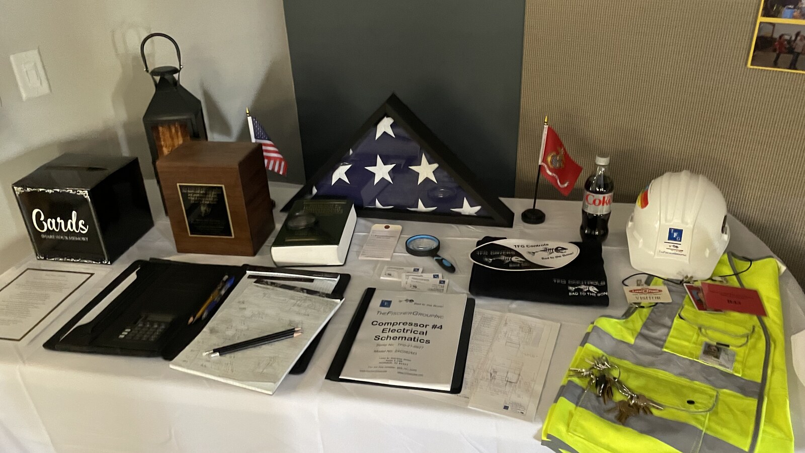 Norm Fischer's folded flag, hard hat, safety vest, electrical schematics, and work papers arranged on a memorial table
