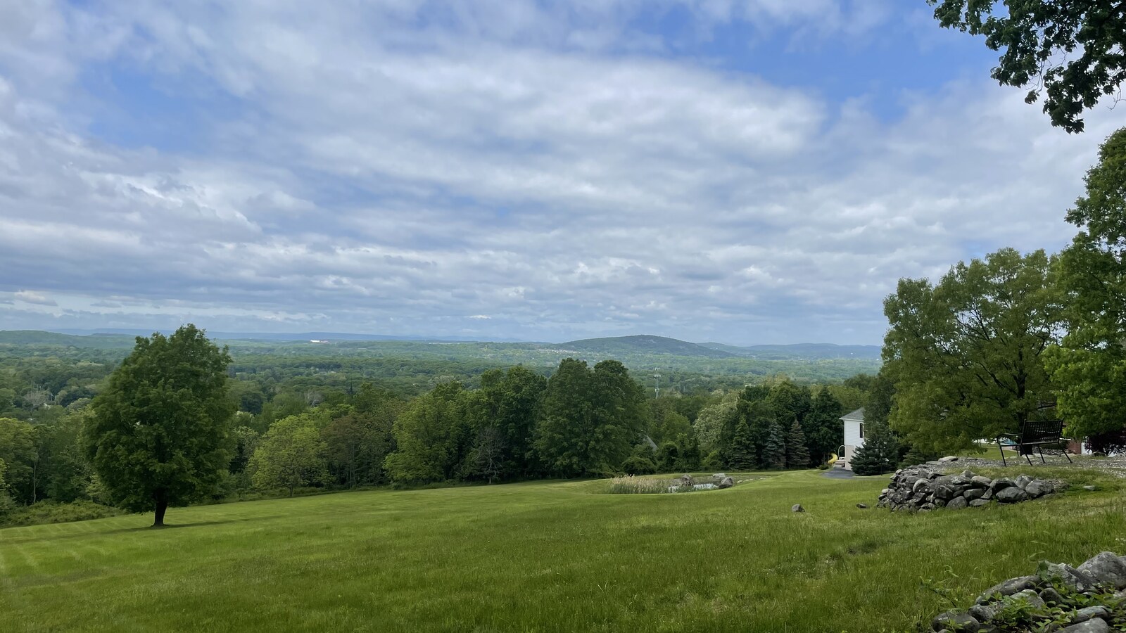 A wide green lawn and wooded Hudson Valley hills beneath a cloudy spring sky
