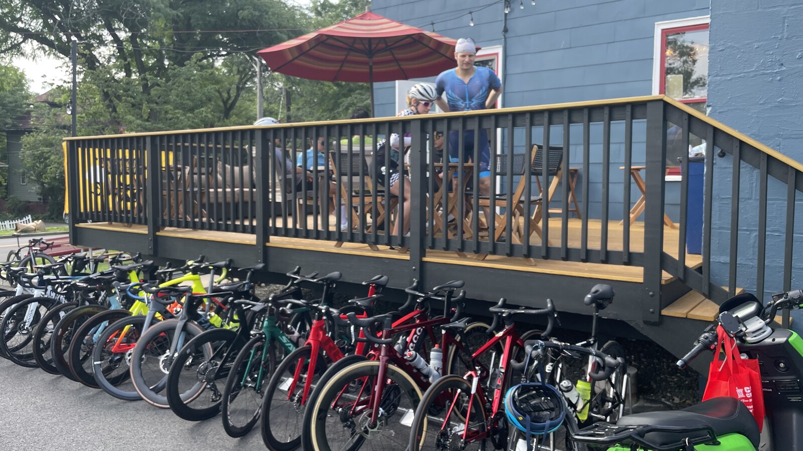 A long row of road bikes parked beneath the deck of a blue building in Piermont