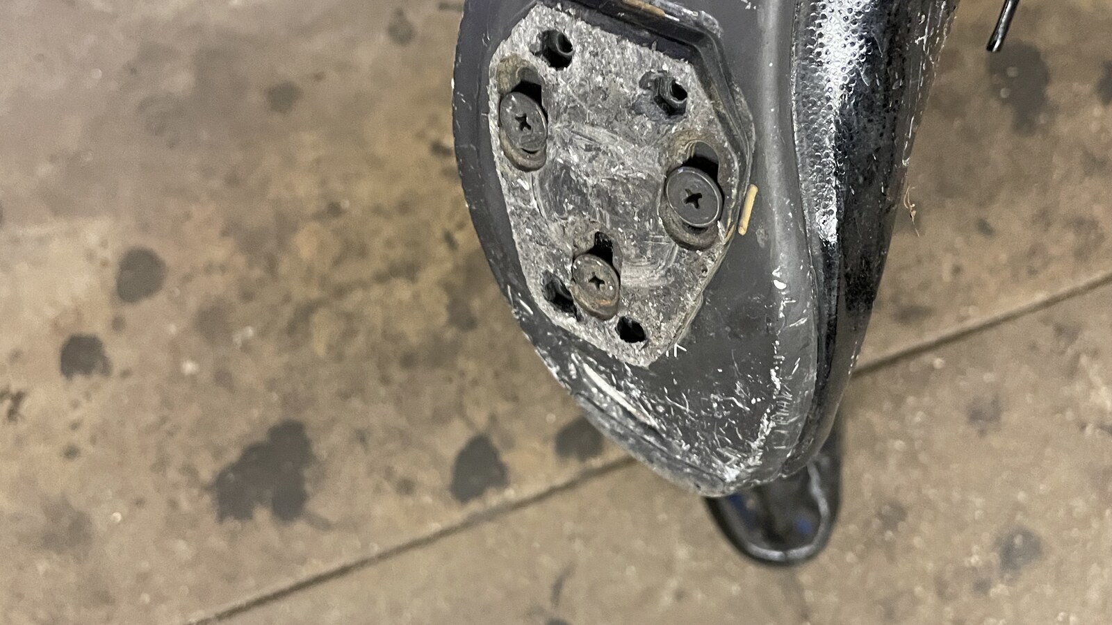The torn sole of a black cycling shoe after its cleat plate ripped away