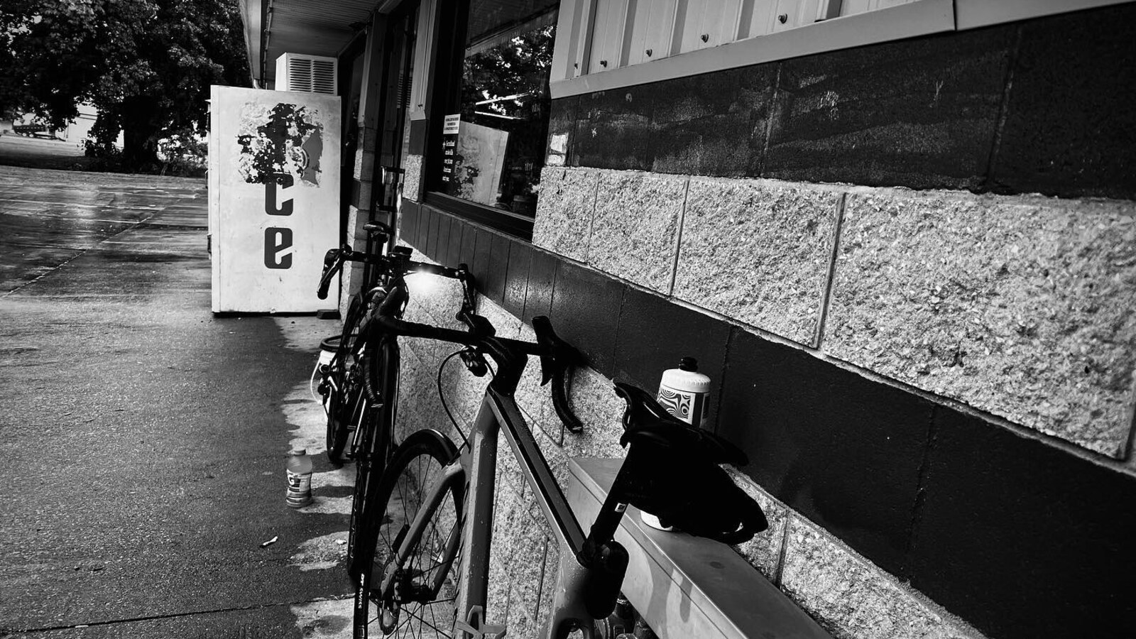Two wet road bikes leaning against a building beside an ice machine