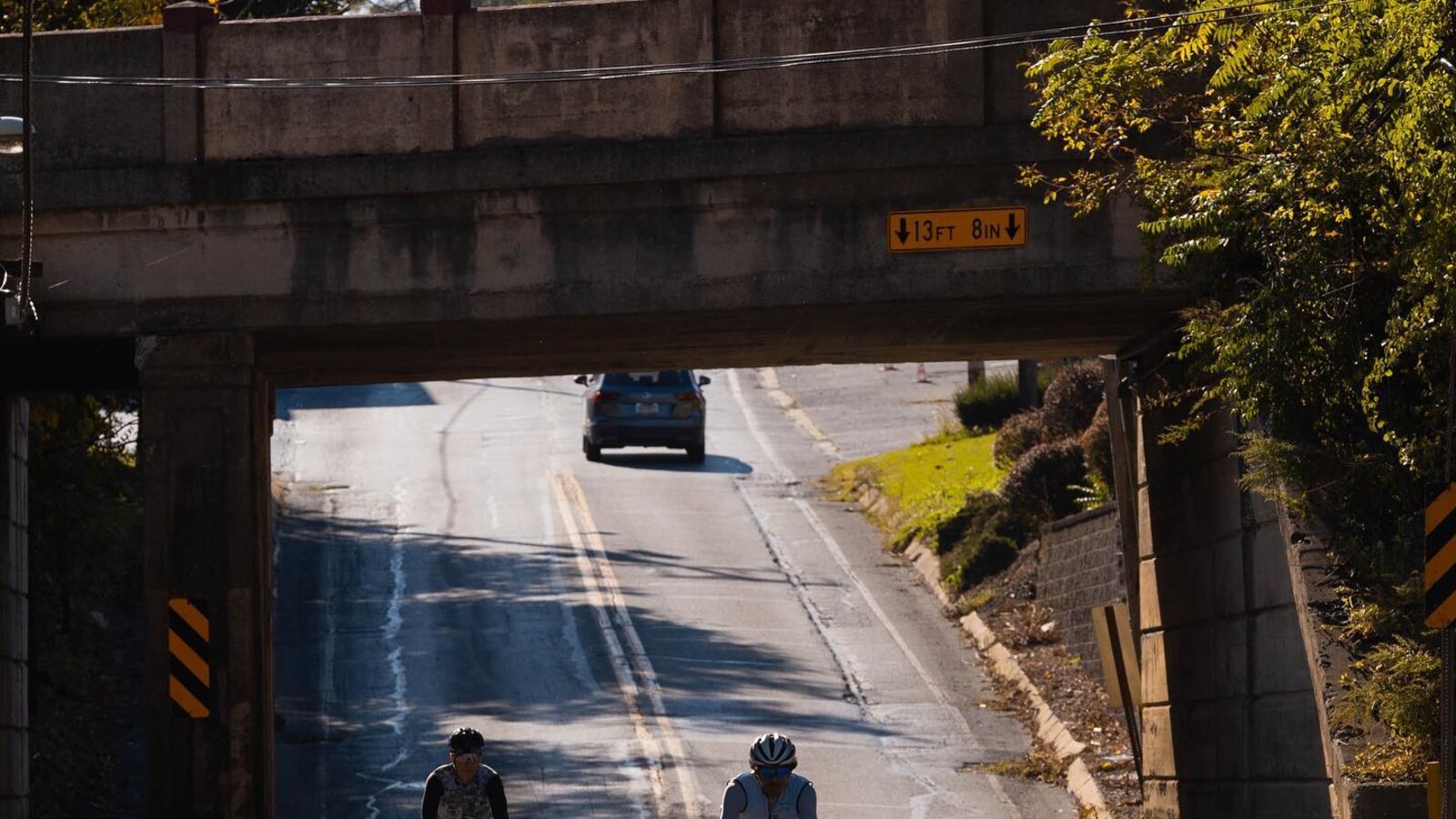 Two cyclists riding uphill beneath a low railroad bridge in New Jersey