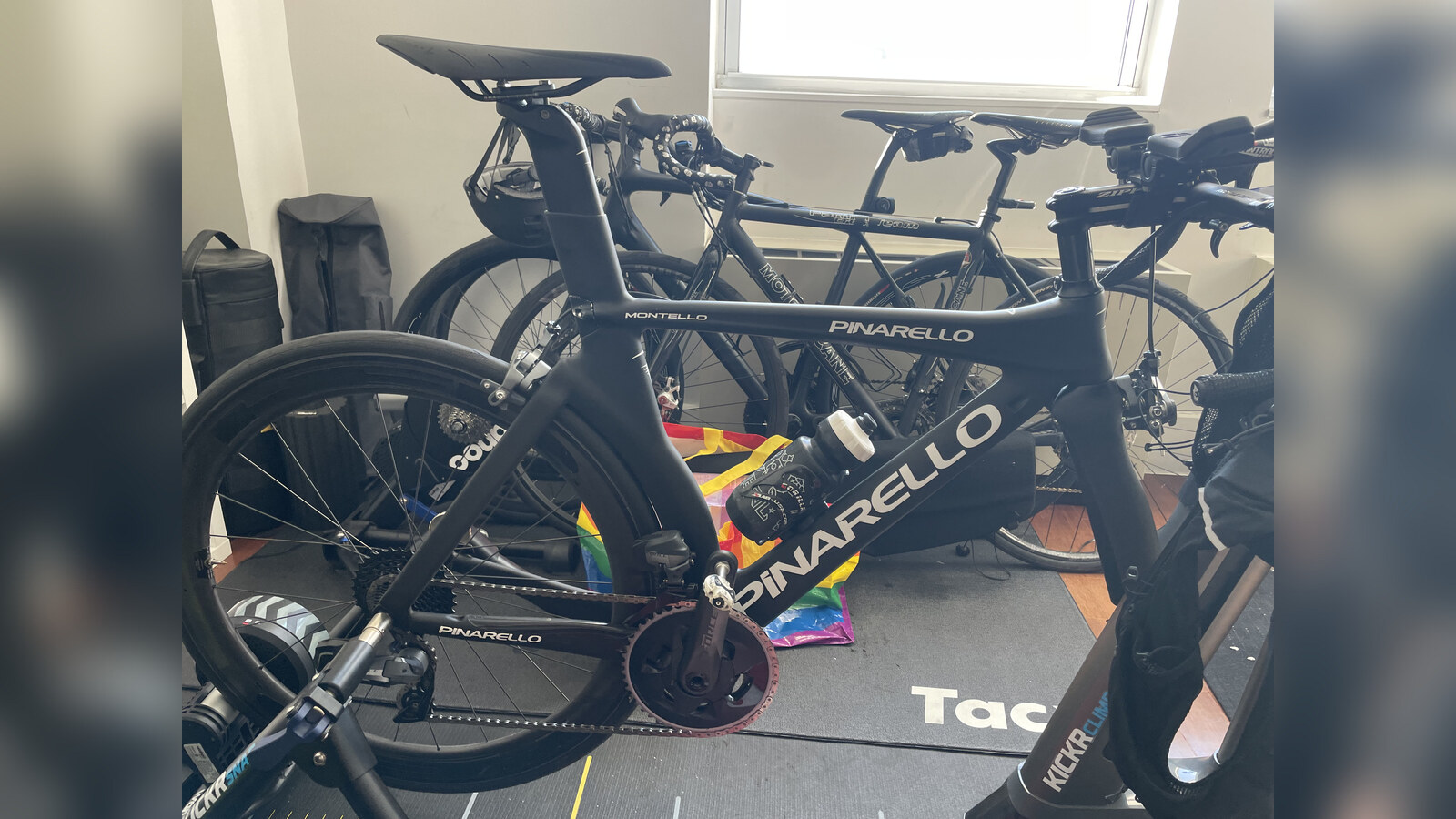 A black Pinarello Montello FM1 time-trial bike set up on an indoor trainer among several other bicycles