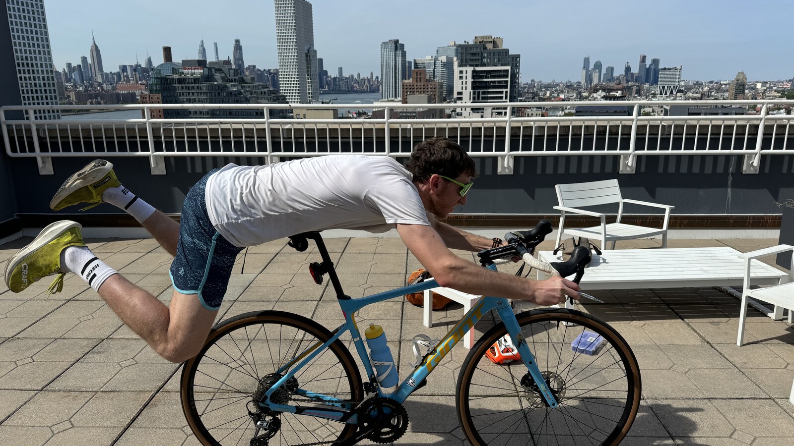 Chris balancing over his bicycle on a Brooklyn rooftop with the Manhattan skyline behind him