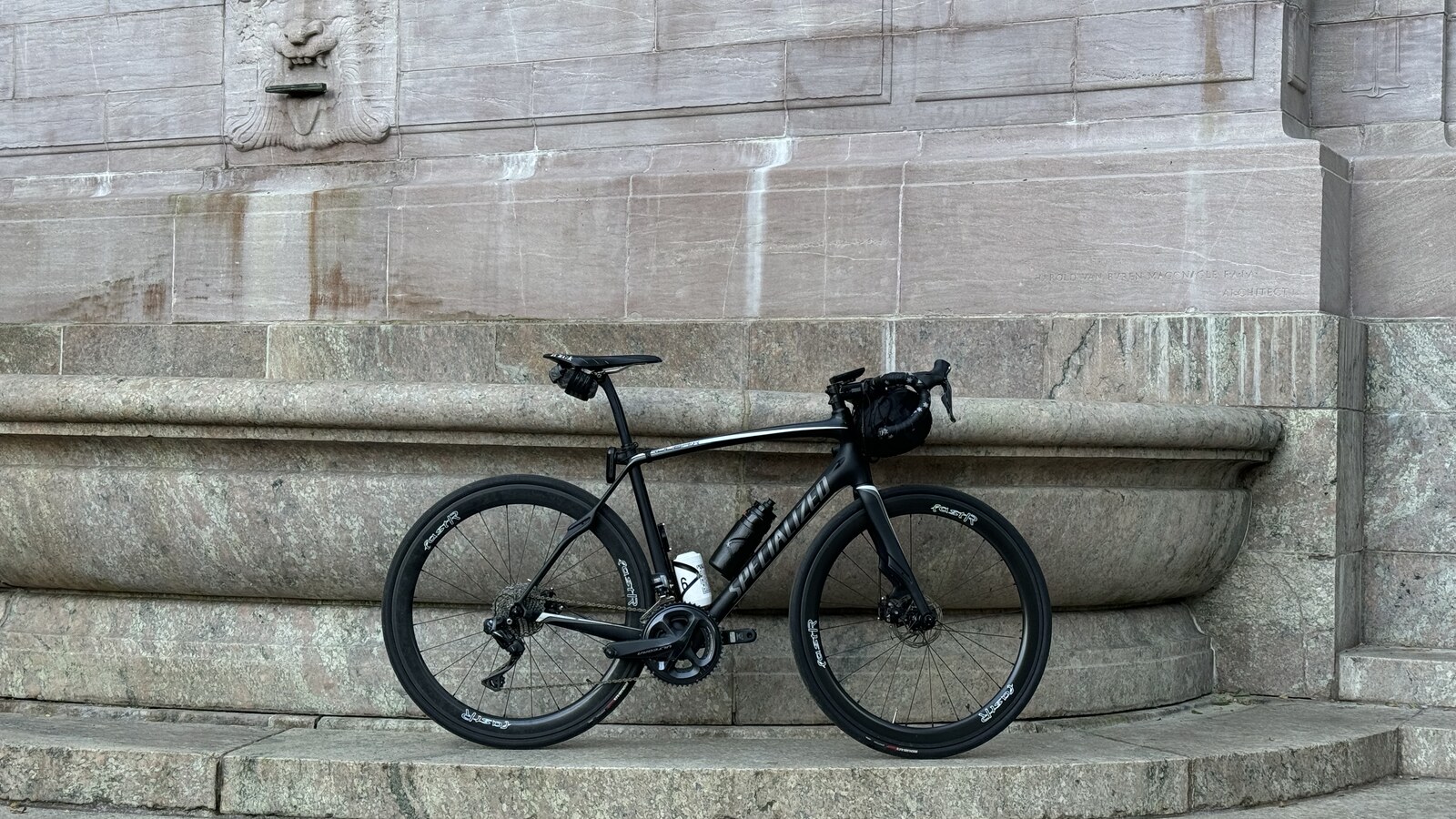 Chris Fischer's black road bicycle resting against a stone monument in New York City